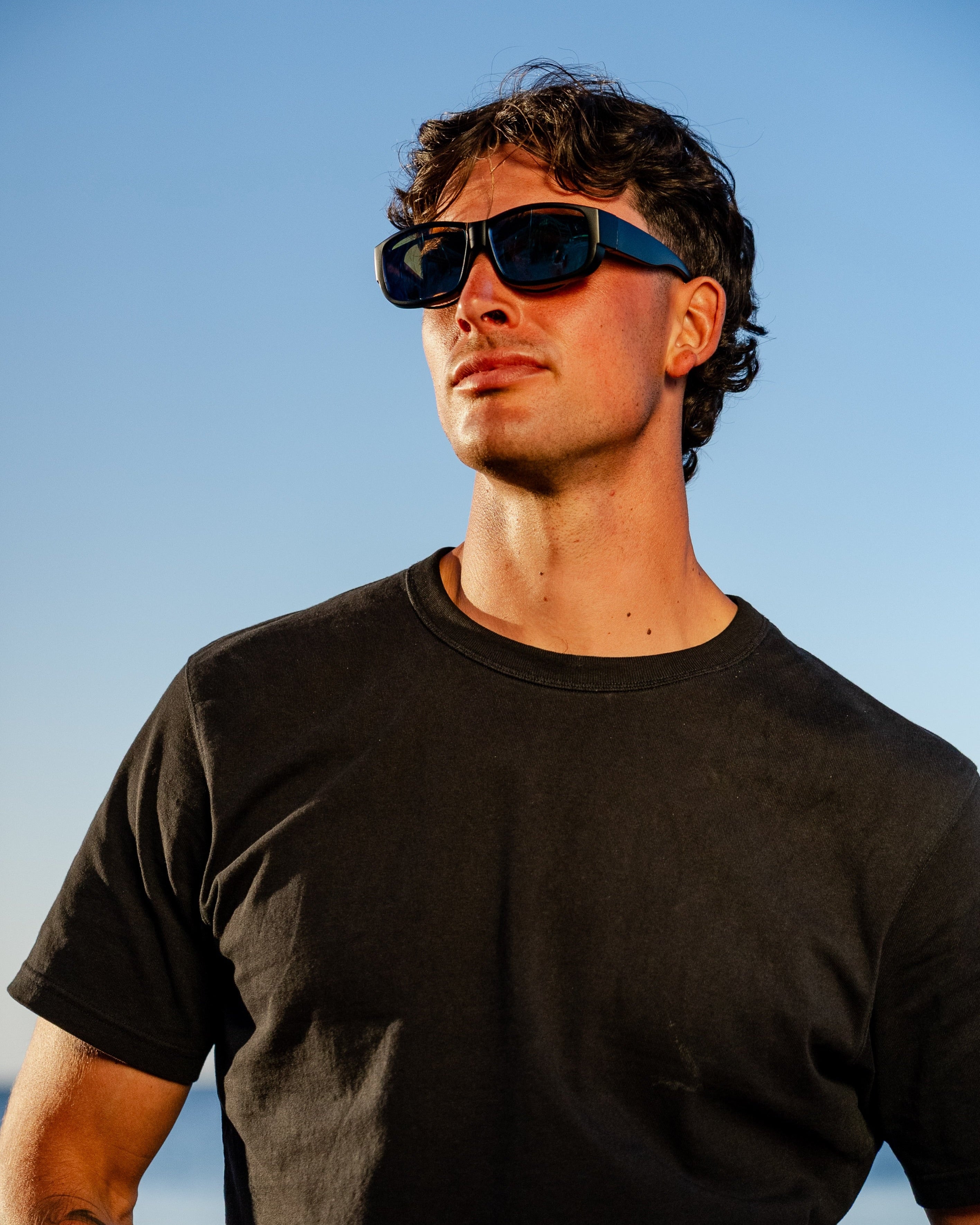 Man wearing sunglasses and a black t-shirt against a clear blue sky