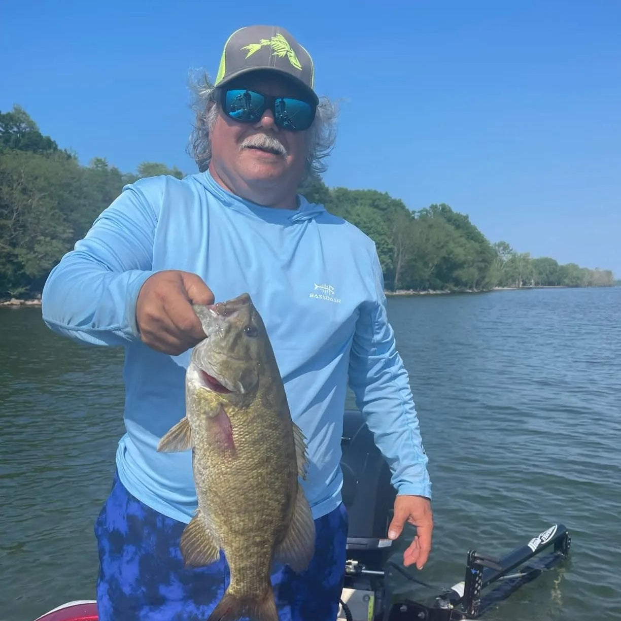 Man holding a fish on a boat by a lake